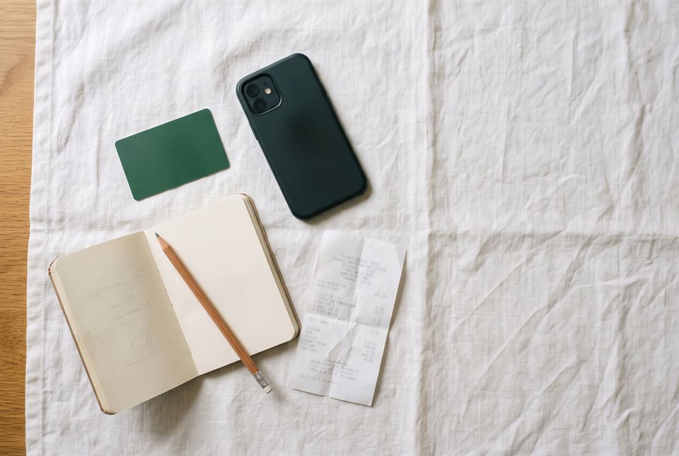 A plain debit card, a smartphone and a notebook laid out on a linen surface