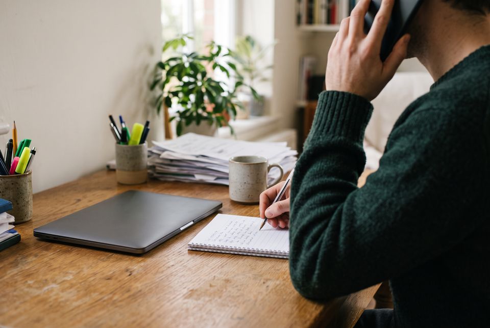 A person making notes on a pad while on a phone call at a home desk